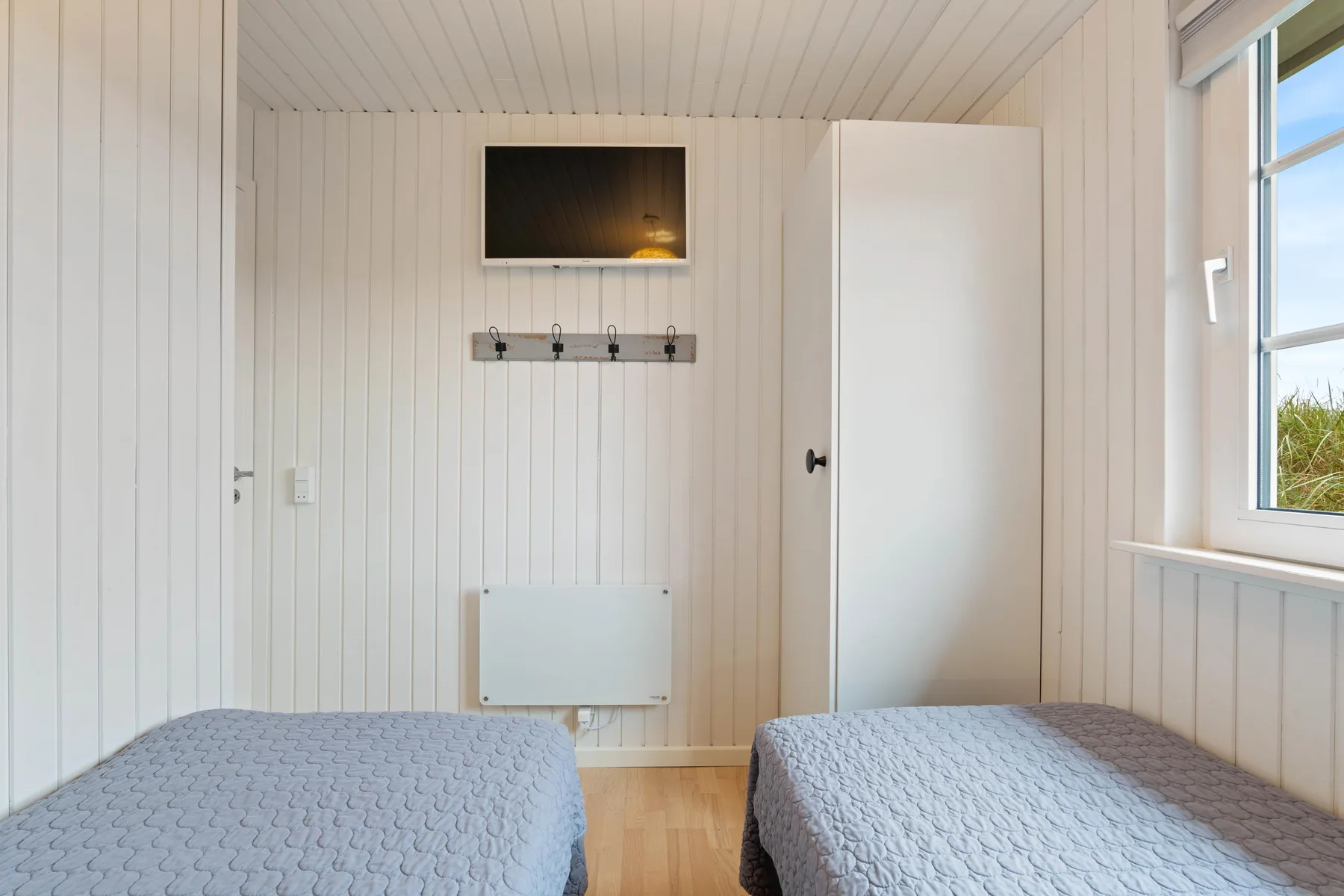 Un dormitorio con dos camas, un televisor en la pared y una ventana.