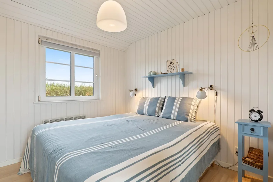Un dormitorio luminoso con una cama vestida con ropa de cama a rayas azules.