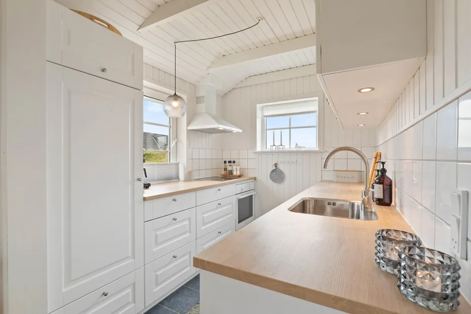 Una cocina luminosa con gabinetes blancos, un fregadero y una encimera de tono madera.