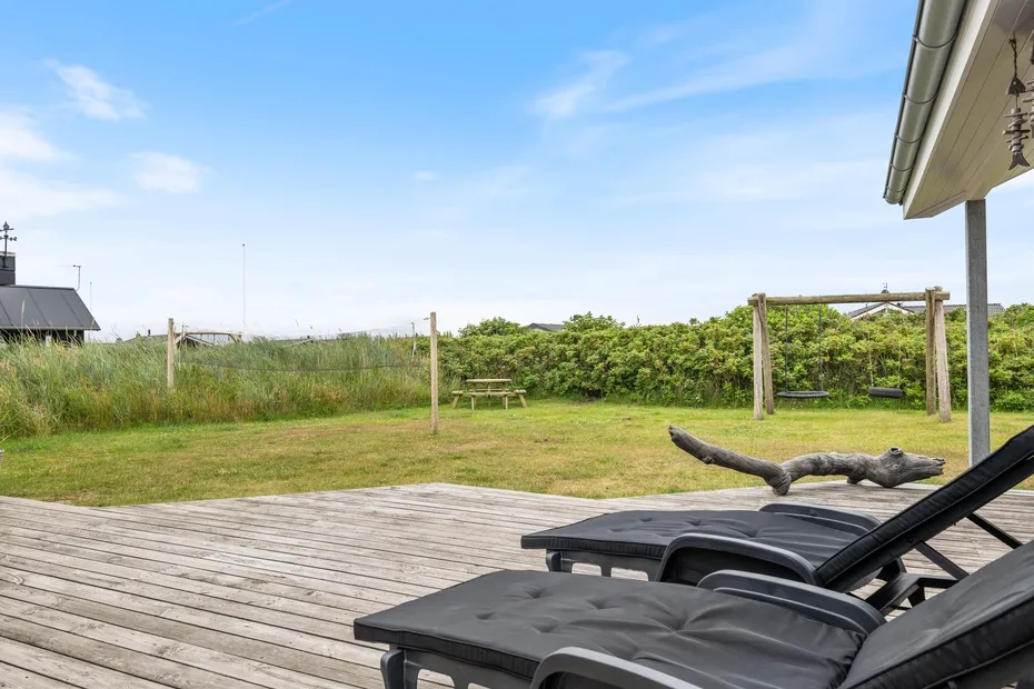 Una terraza exterior con asientos reclinables da a un jardín y un patio con césped.