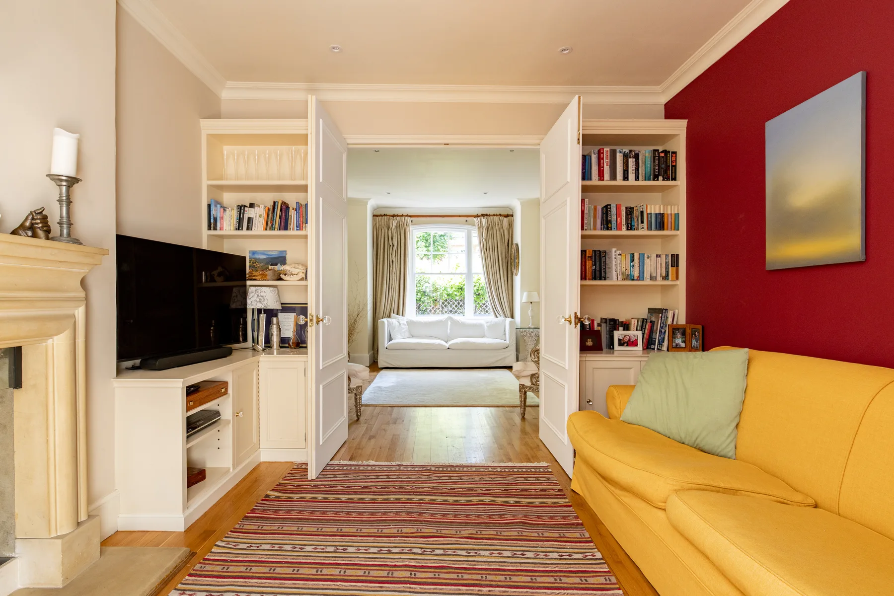 A living room with a yellow sofa, television, and open doors to a bright adjoining room.