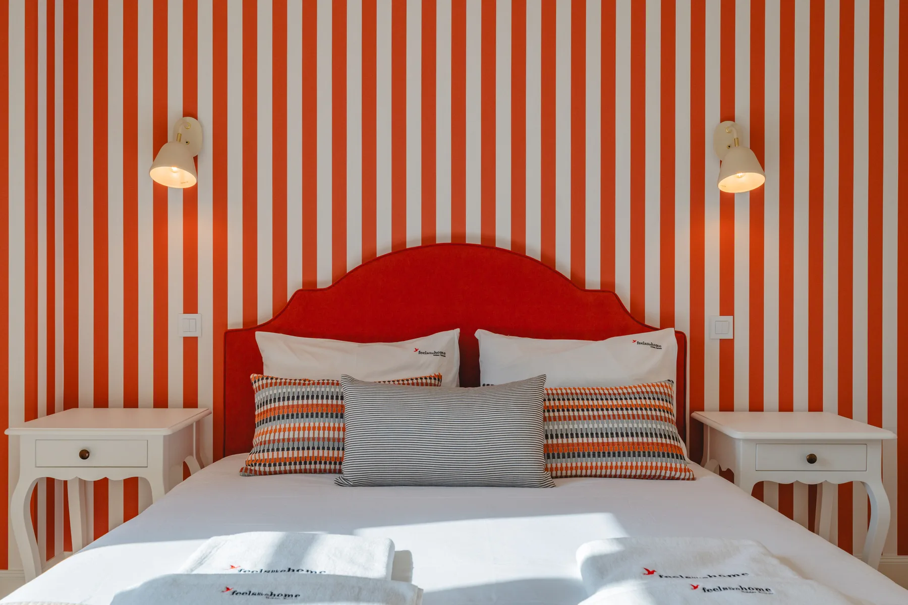 A bedroom with a bed against a red-and-white striped wall.