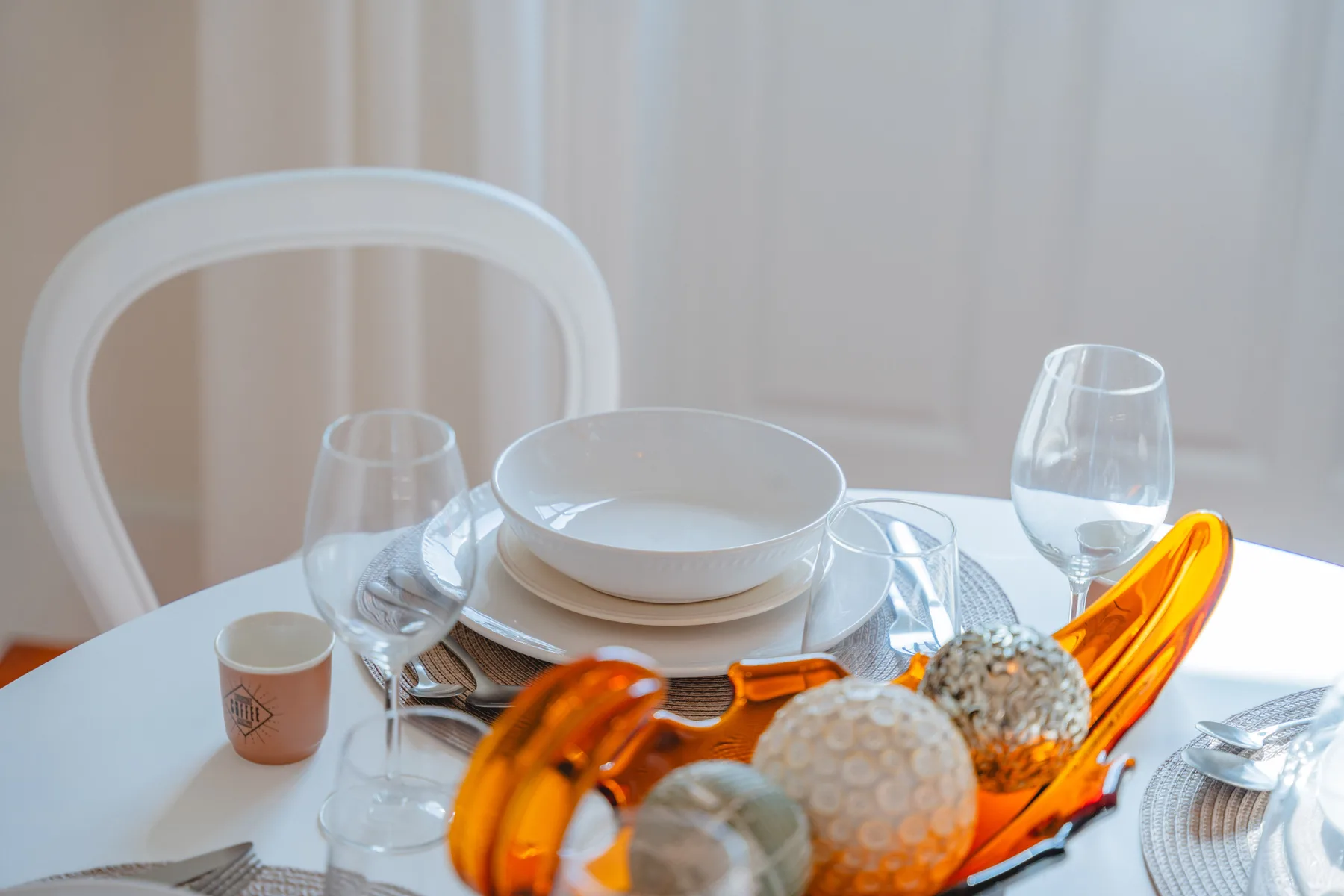 A dining table is set with plates, glasses, and orange decorative pieces.