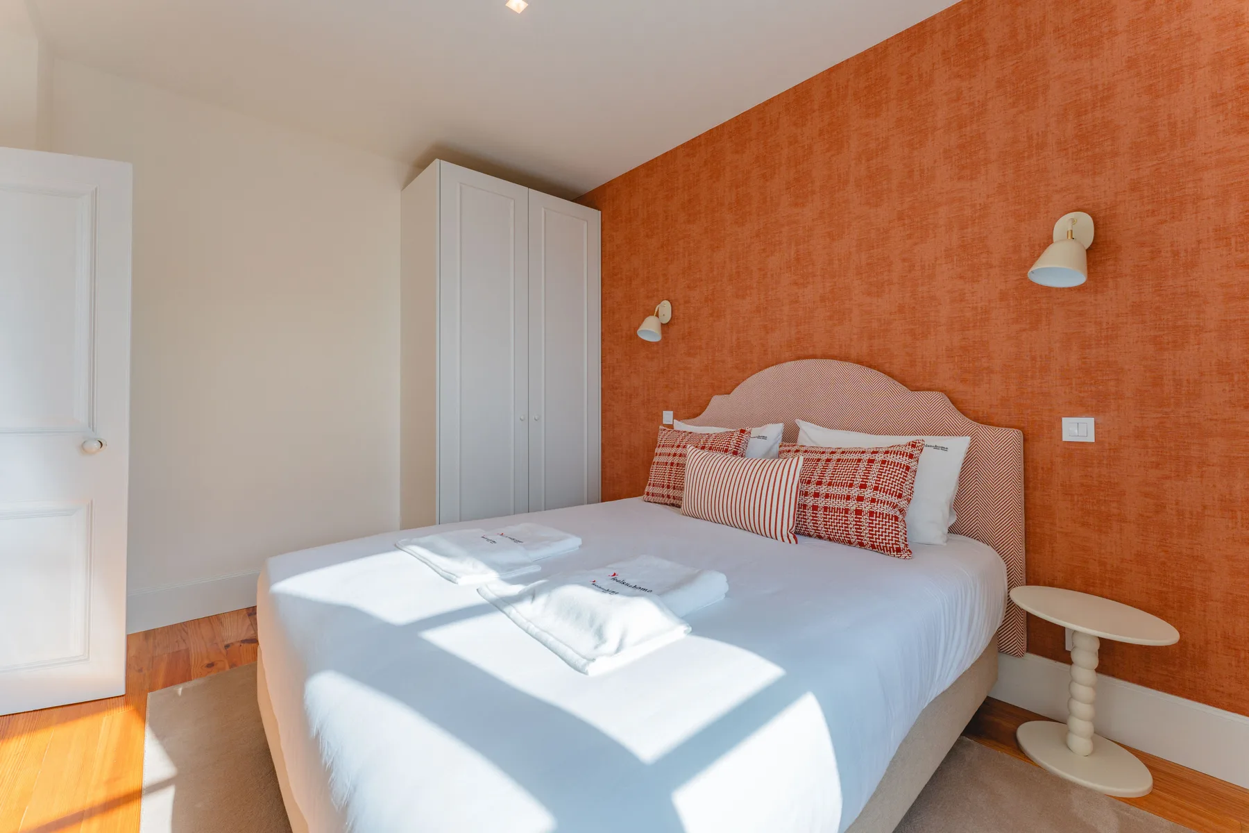 Un dormitorio con una cama vestida con ropa blanca y cojines estampados.