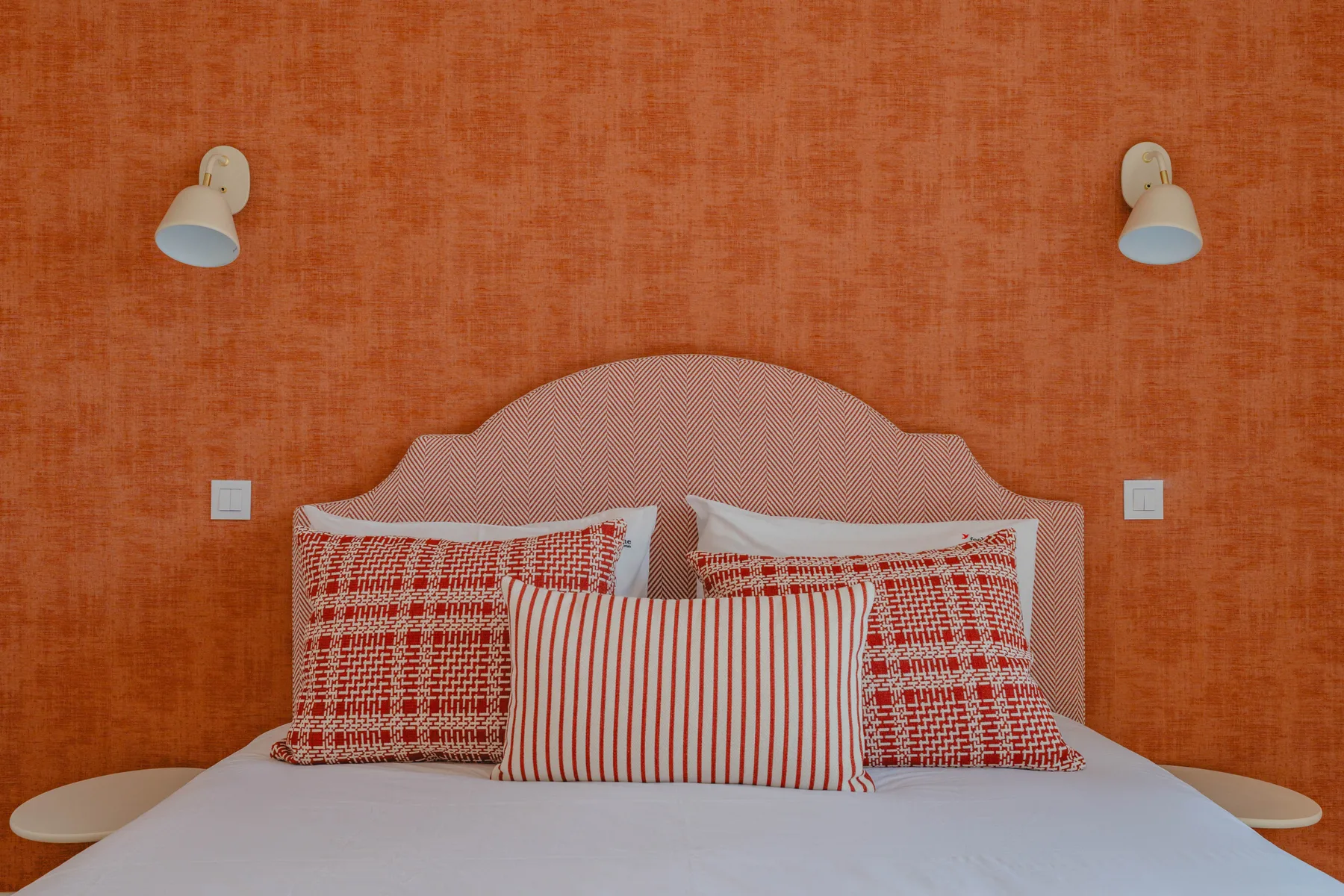 A bedroom with a bed against an orange wall and patterned pillows.