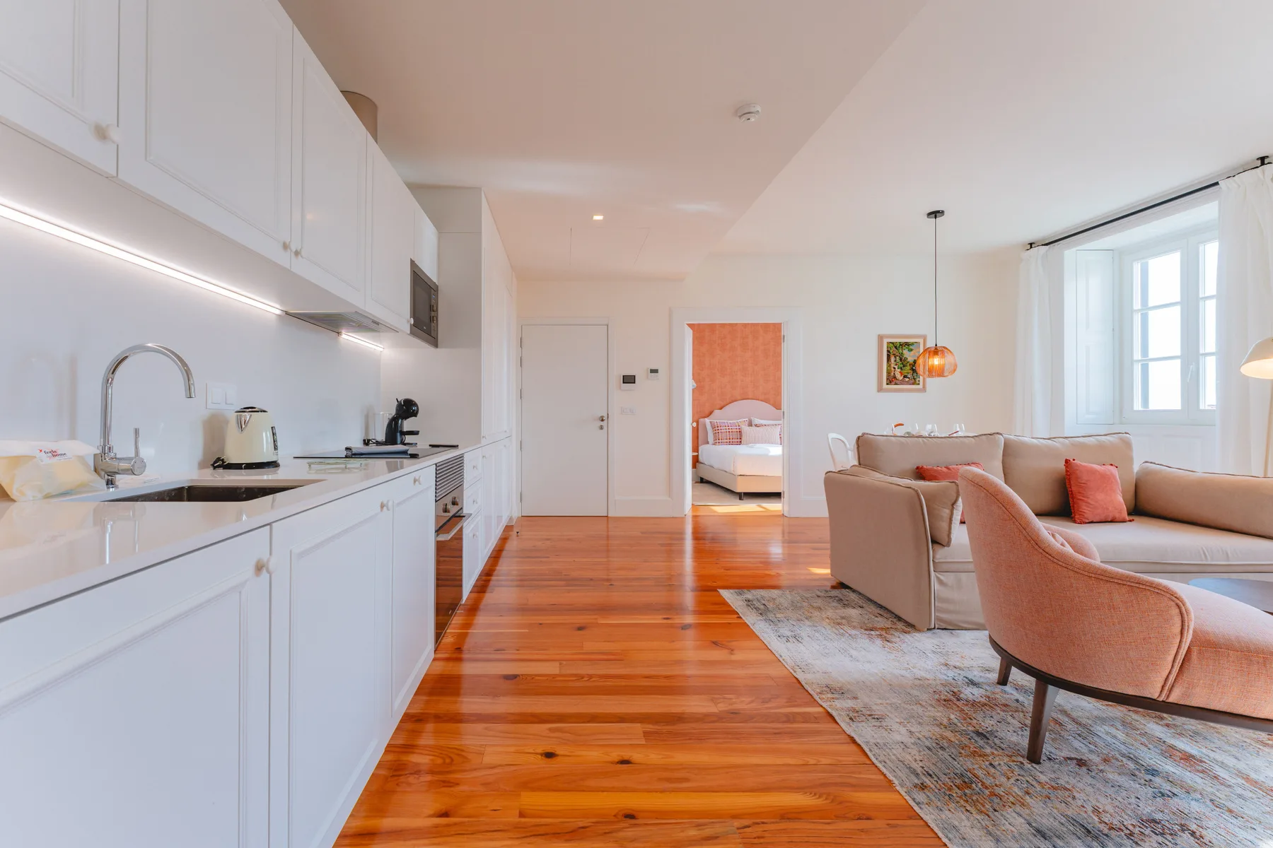 A bright open-plan living room and kitchen with warm wood flooring and seating.