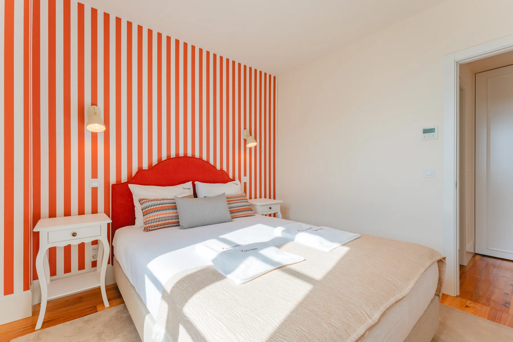 A bright bedroom with a bed against a red-and-white striped wall.