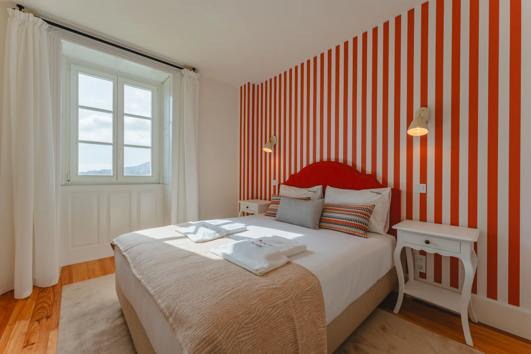 Un dormitorio con una cama frente a una pared de rayas rojas y blancas.
