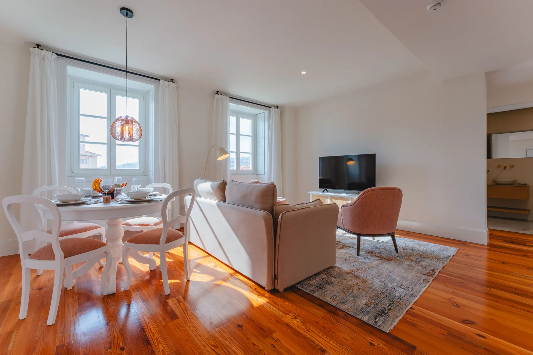 A bright living and dining area with seating, a table, and a television.