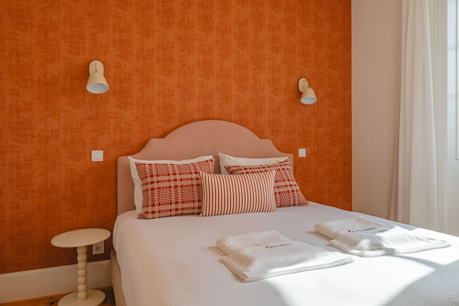 A bedroom with a bed dressed in patterned pillows and folded towels.