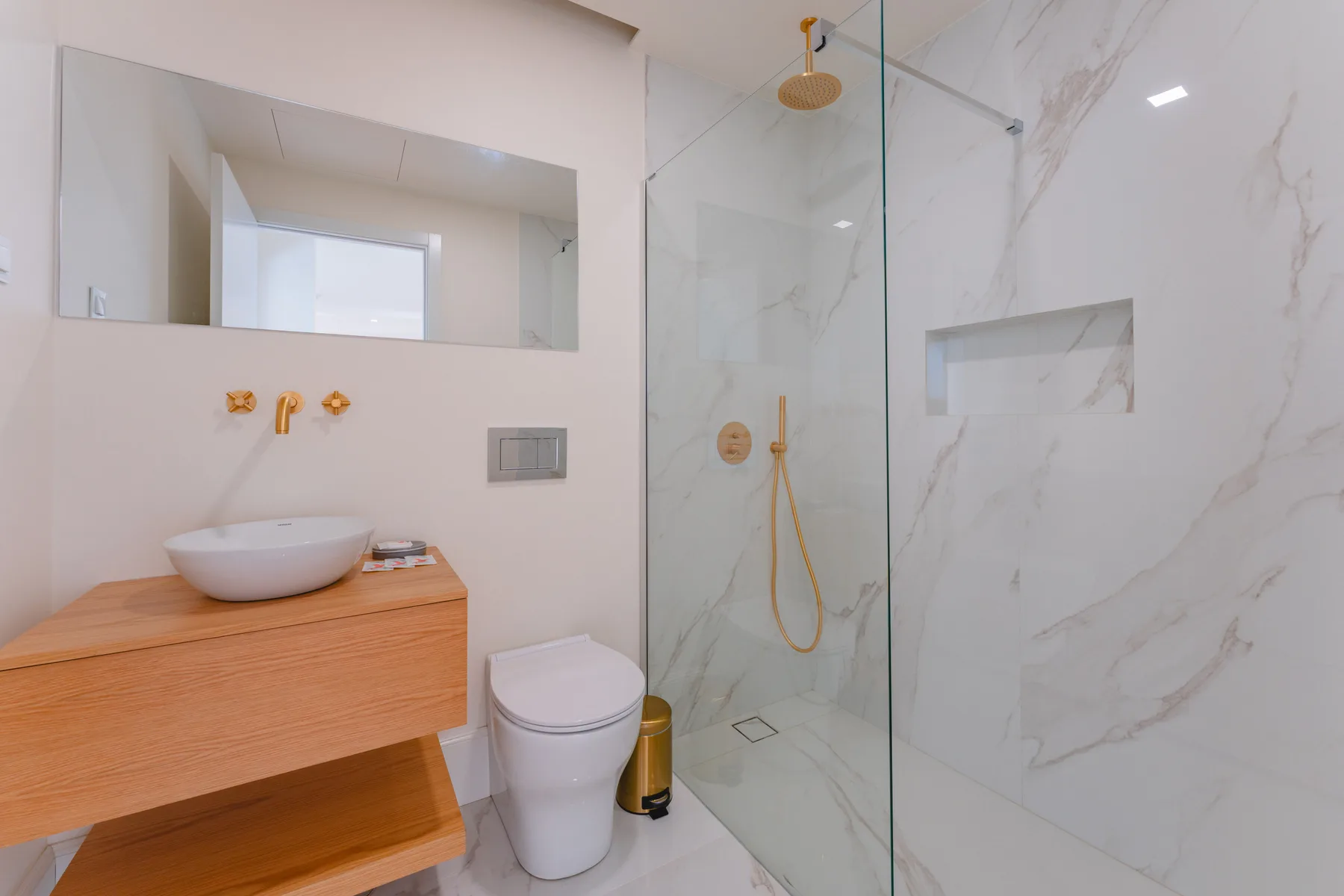 A modern bathroom with a wood vanity, toilet, and glass shower.