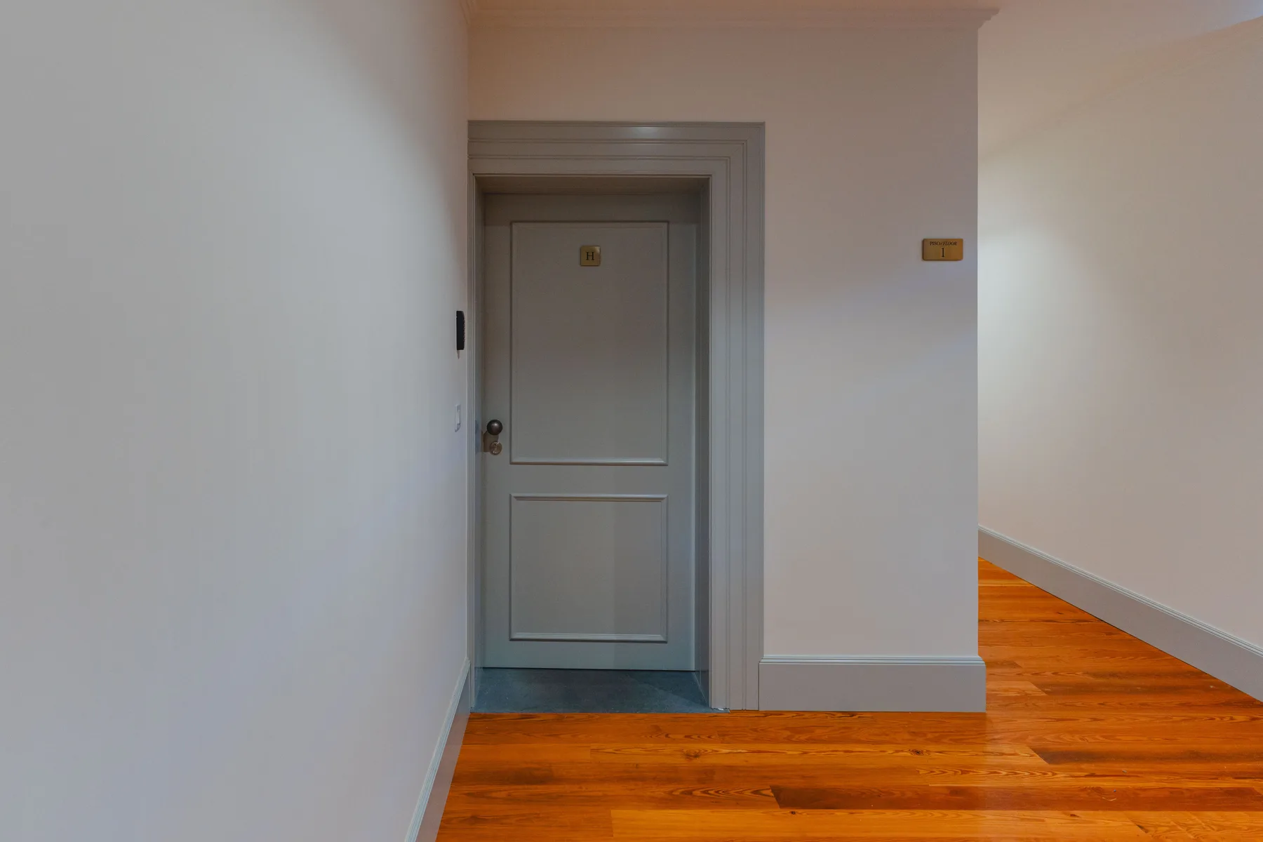 A hallway with a closed door and warm wood flooring.
