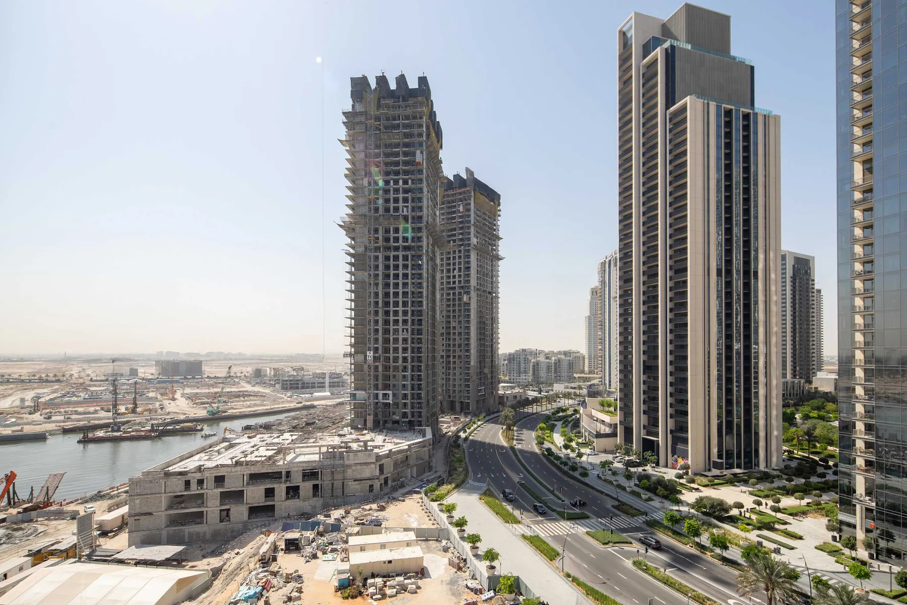 Urban cityscape with high-rise buildings, including a tower under construction beside a curving road.