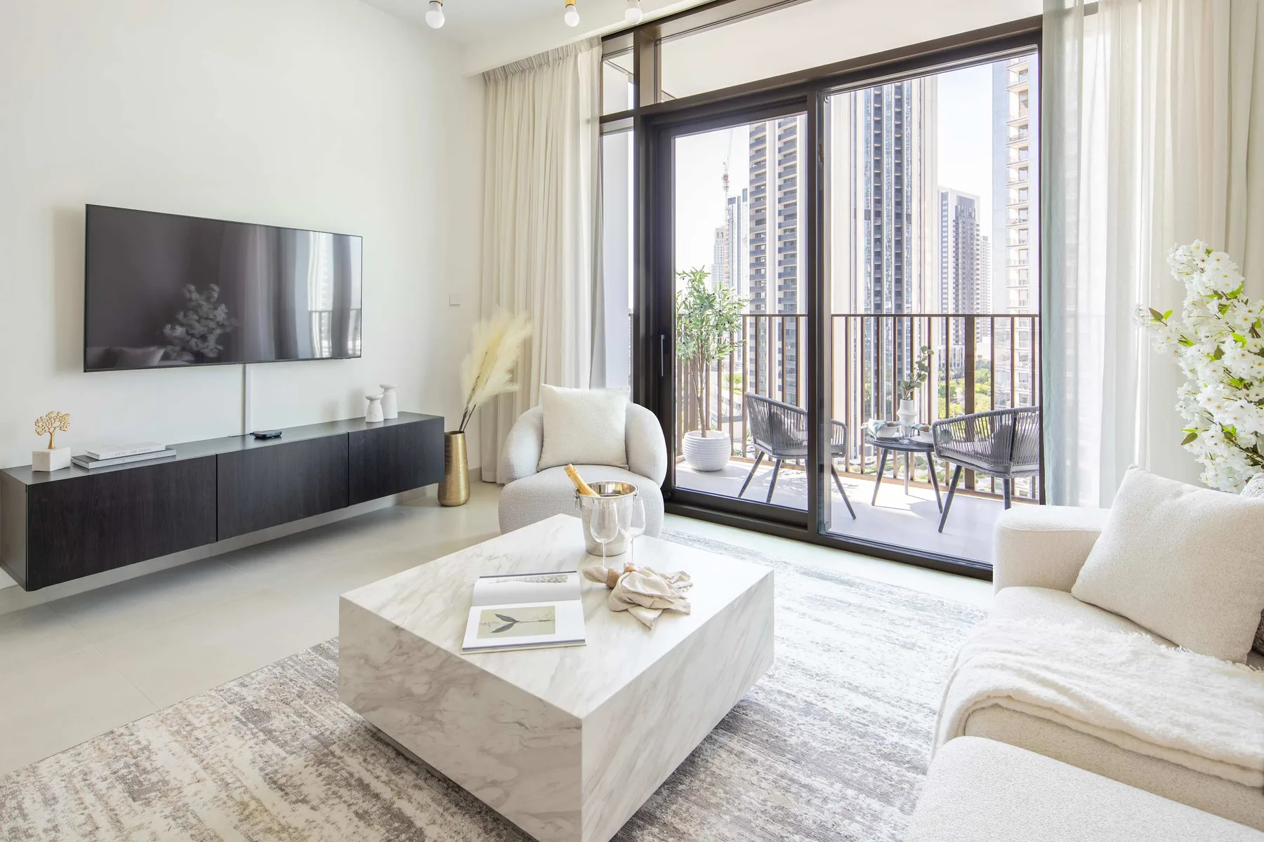 Una sala luminosa con televisor, asientos y grandes ventanales que dan a un balcón.