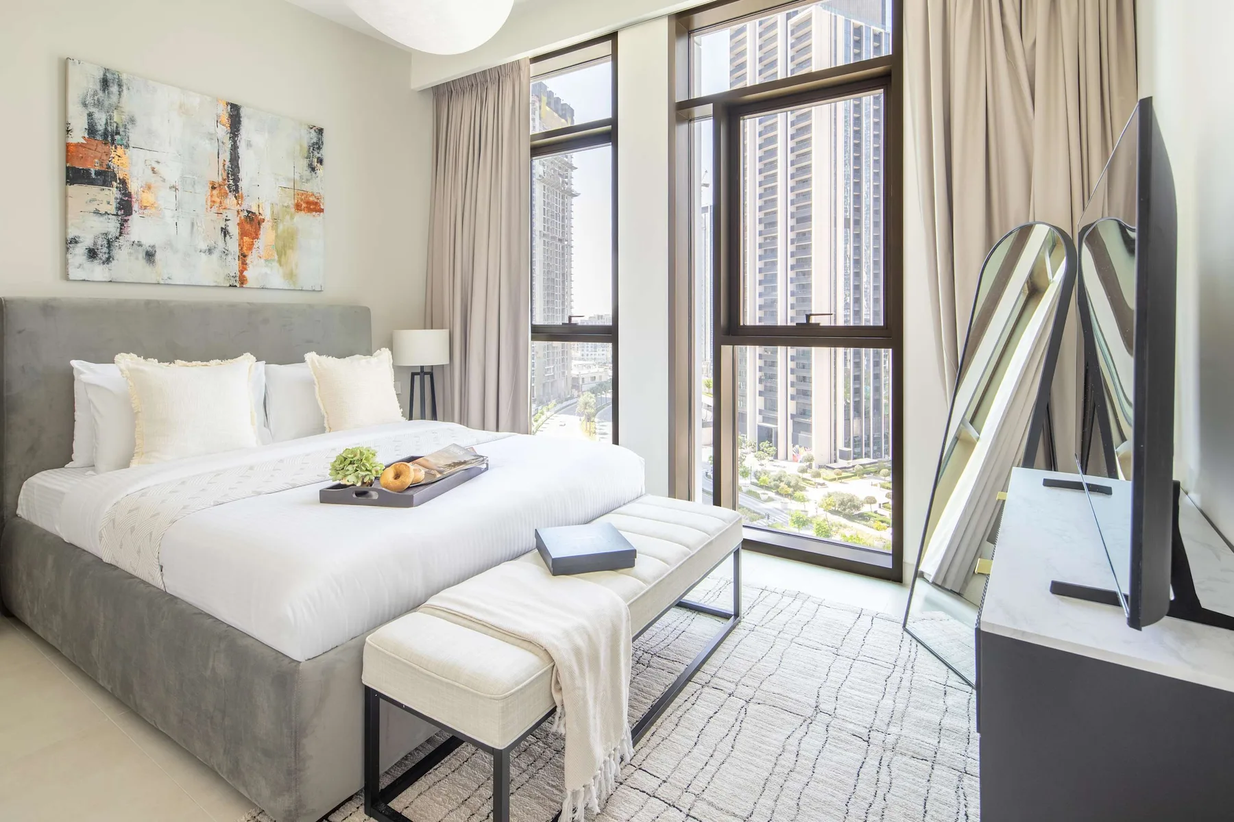 A bright bedroom with a neatly made bed beside tall windows.