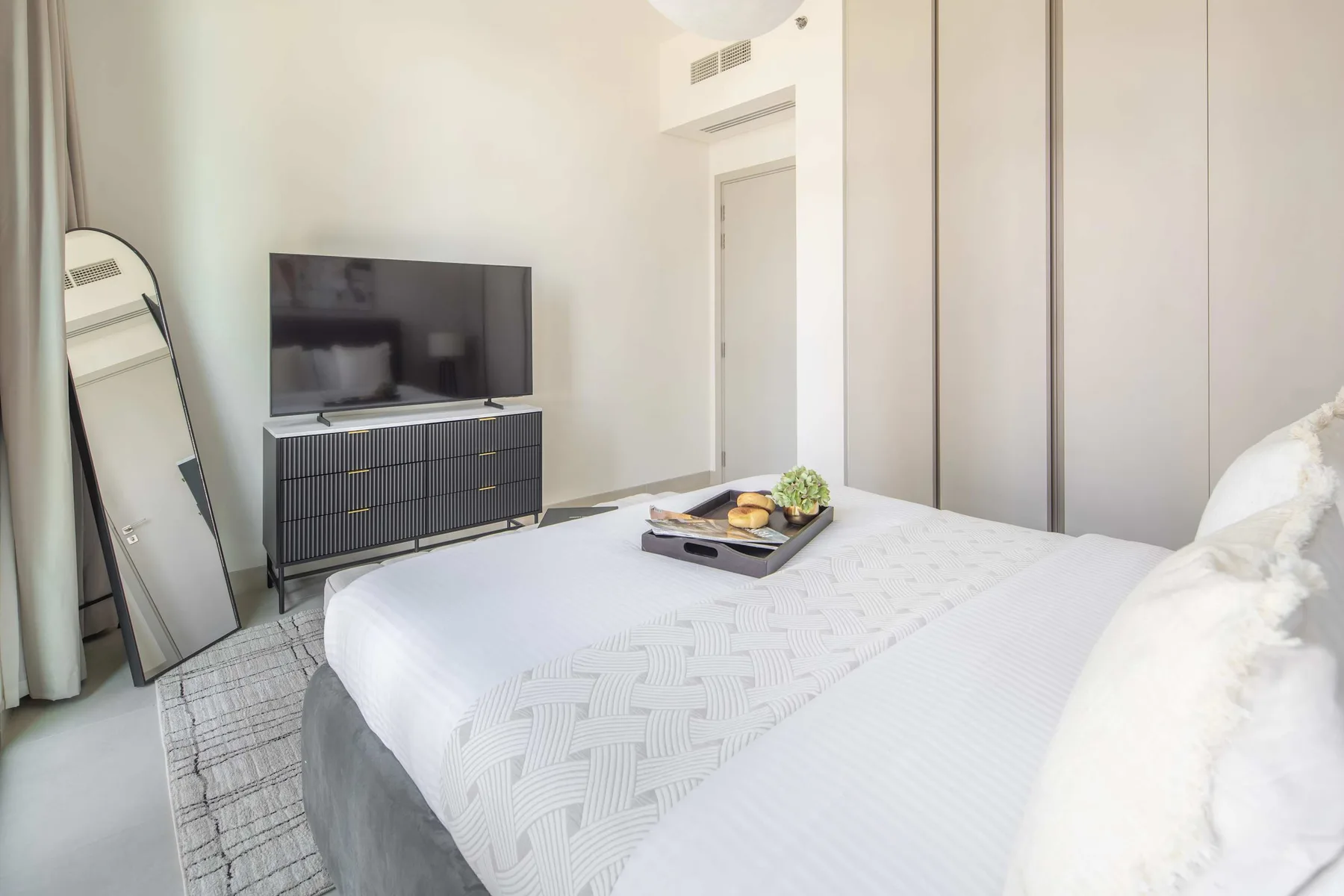 A bright bedroom with a neatly made bed and a television on a cabinet.