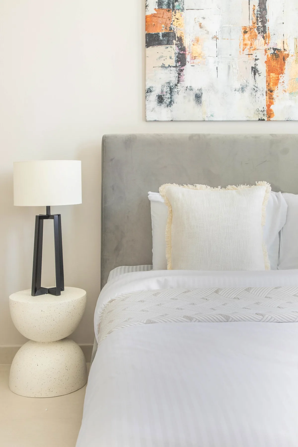 A bedroom with a neatly made bed, gray headboard, and bedside lamp.
