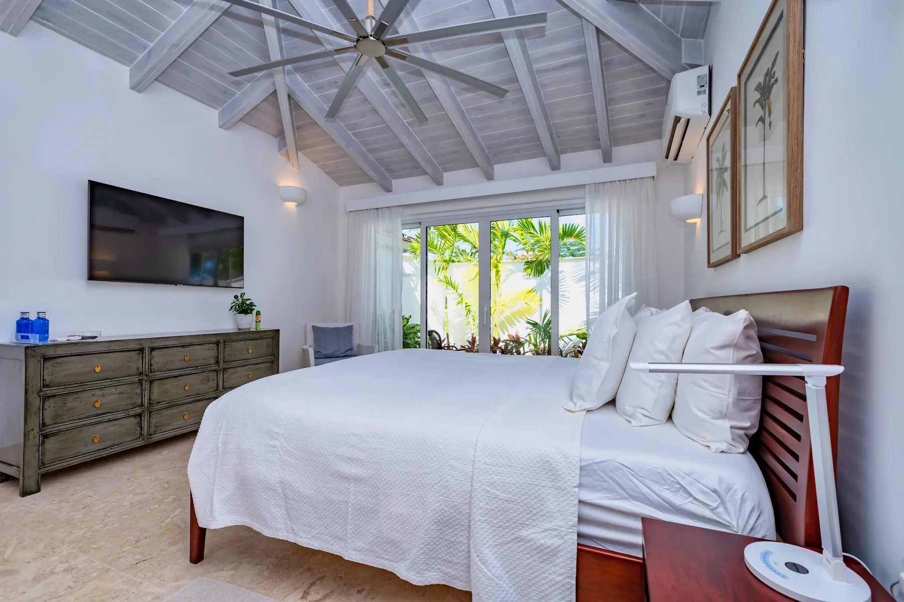 A bedroom with a large bed, wall-mounted television, and windows overlooking greenery.
