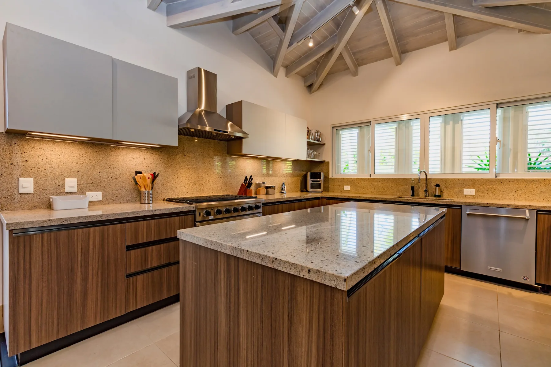 A spacious kitchen with a central island, wood cabinetry, and windows along the counter.