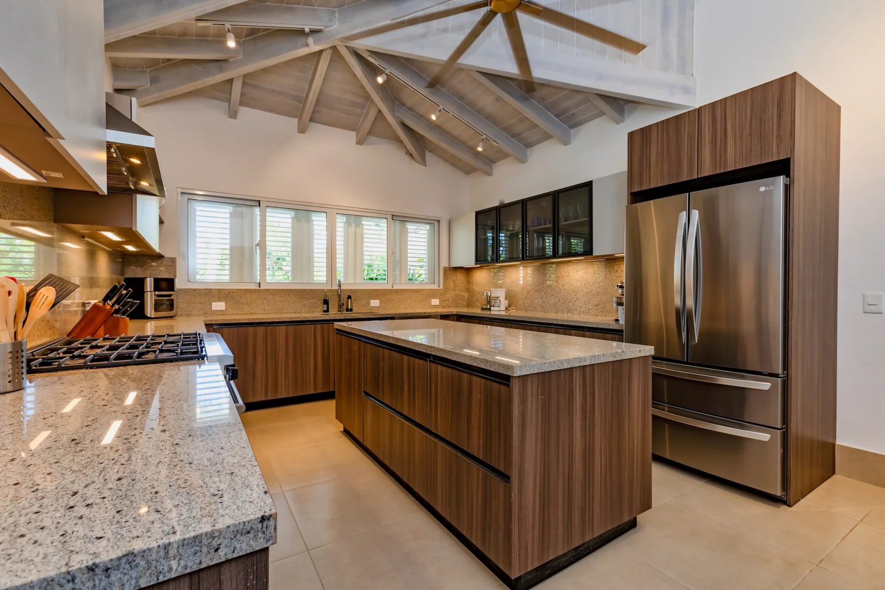 A spacious kitchen with a central island, stainless steel refrigerator, and exposed ceiling beams.