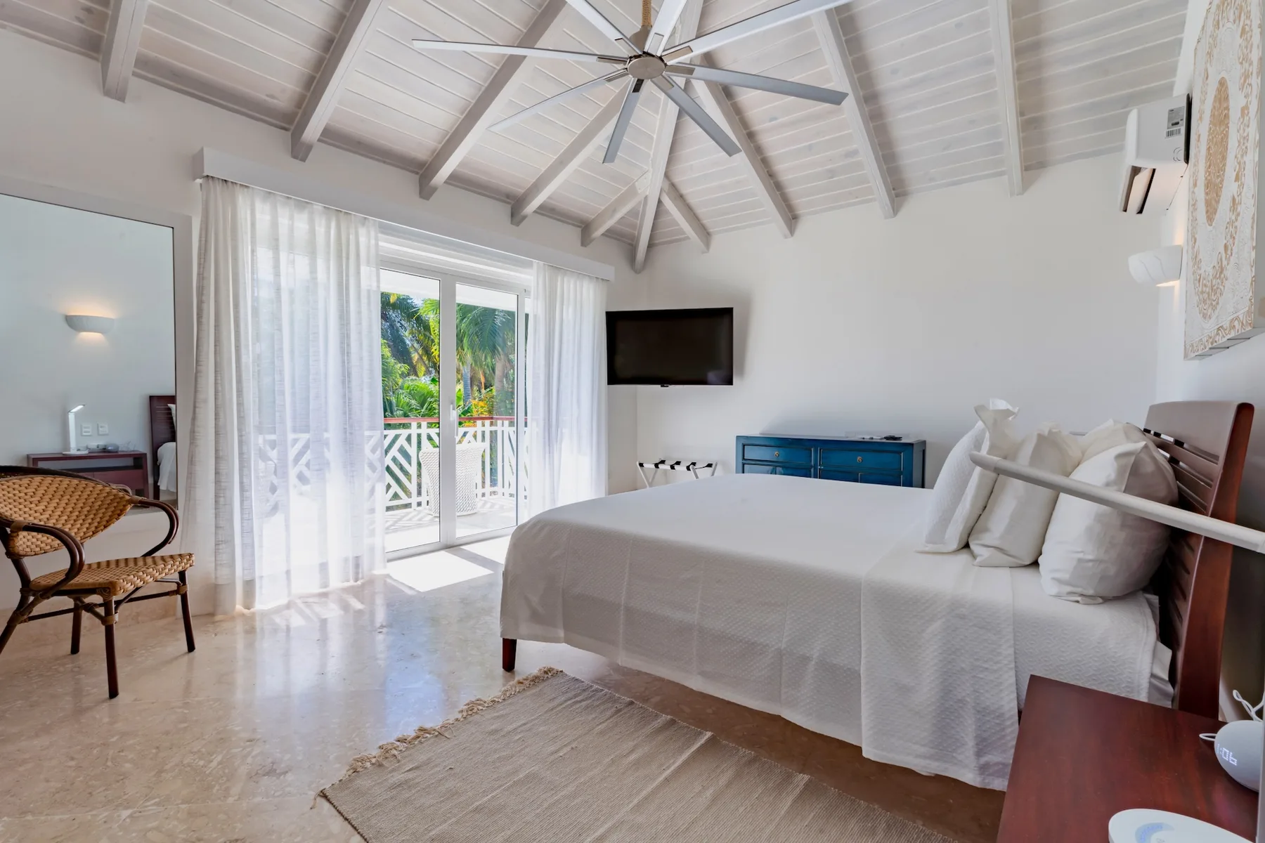 A bright bedroom with a bed beside glass doors opening to a balcony.