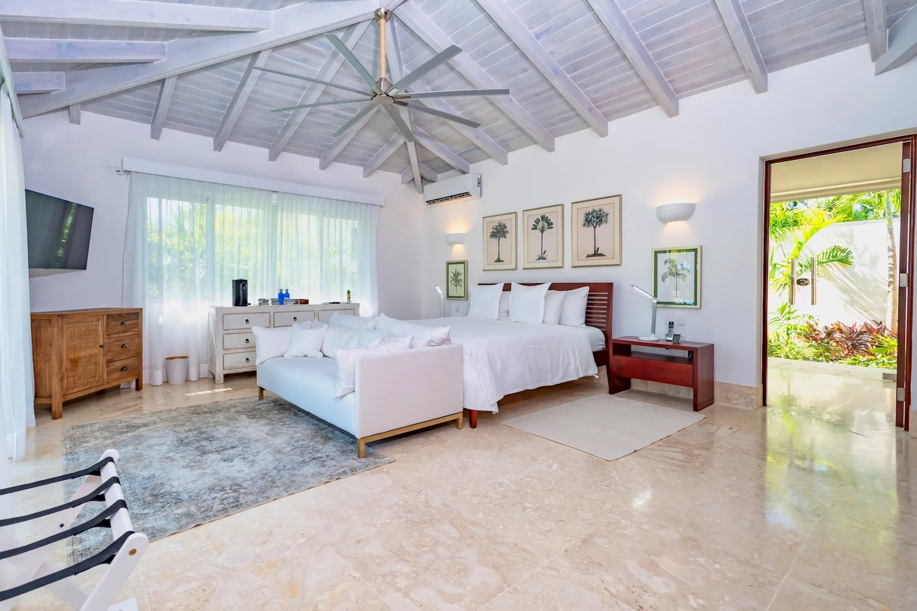A bright bedroom with two beds beneath a high, beamed ceiling.