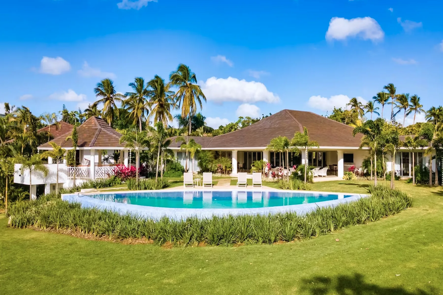Tropical resort scene with a swimming pool in front of low buildings and palm trees.