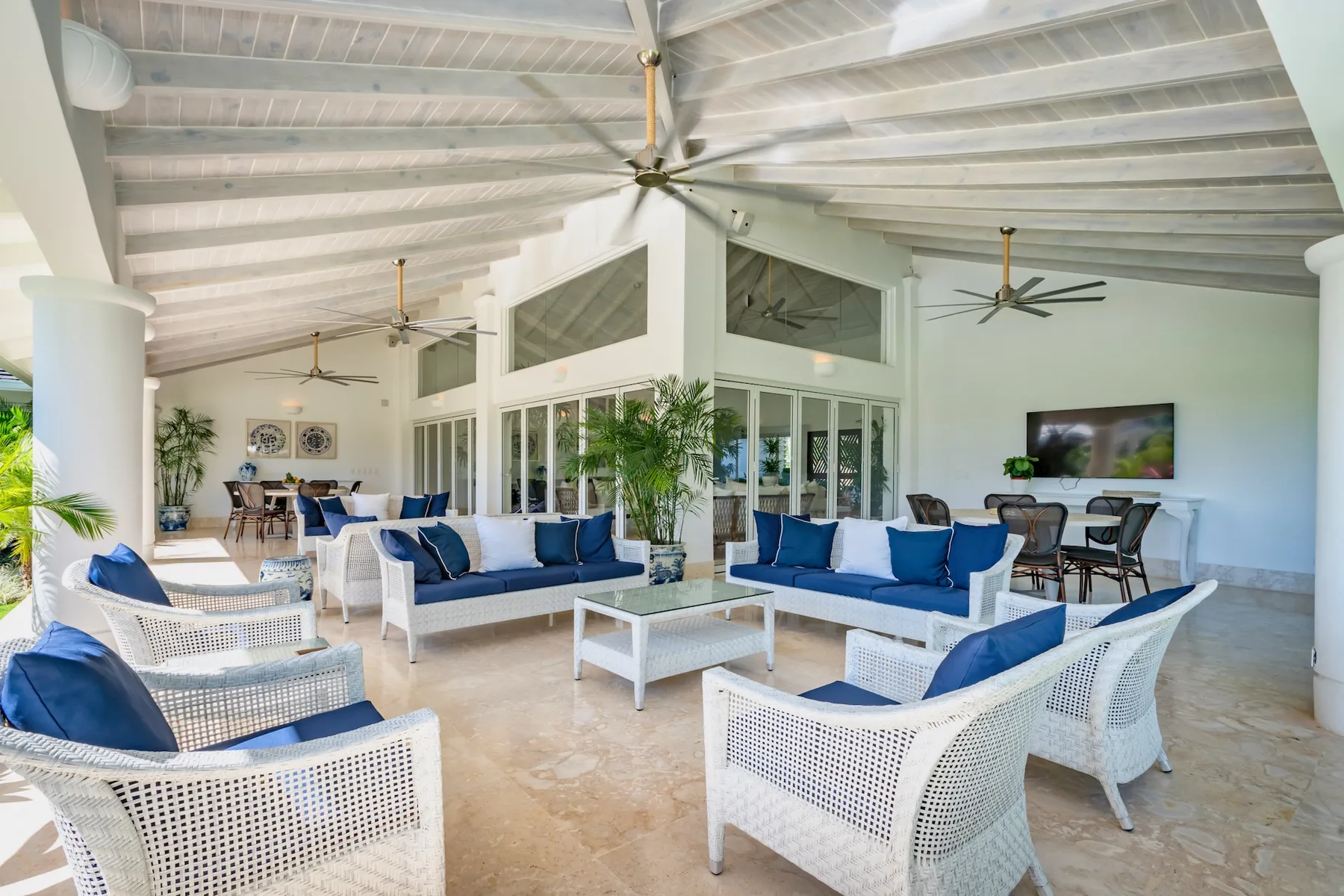 A bright open-plan lounge with white seating, blue cushions, and a dining area.