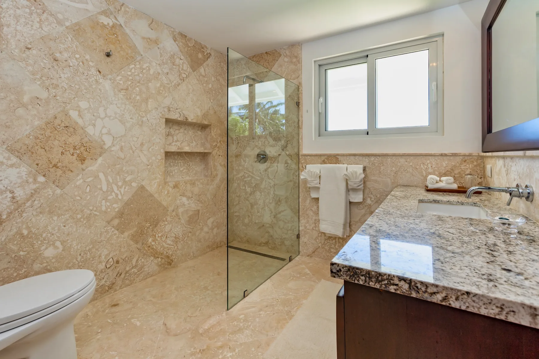 A tiled bathroom with a glass shower and a stone countertop.