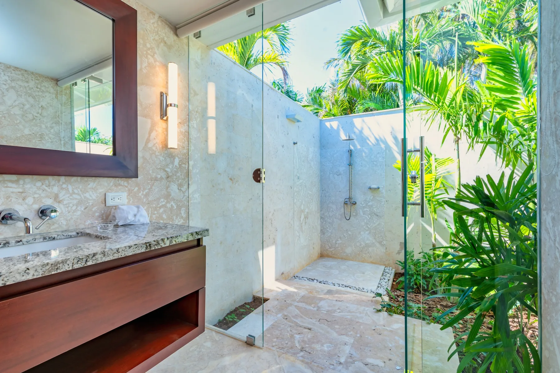 A bright bathroom with a glass-enclosed shower opening onto lush tropical greenery.
