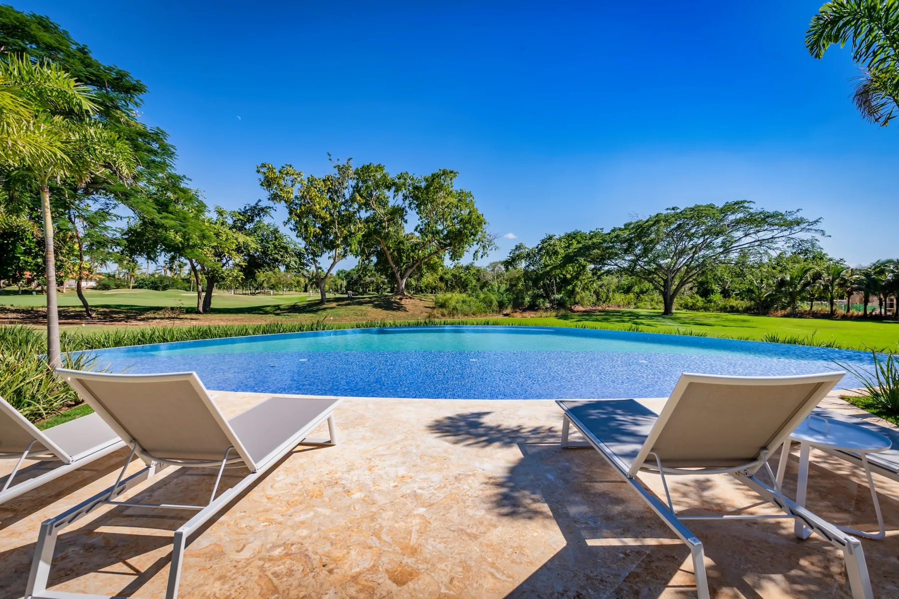 An outdoor swimming pool with lounge seating, surrounded by green trees and lawn.