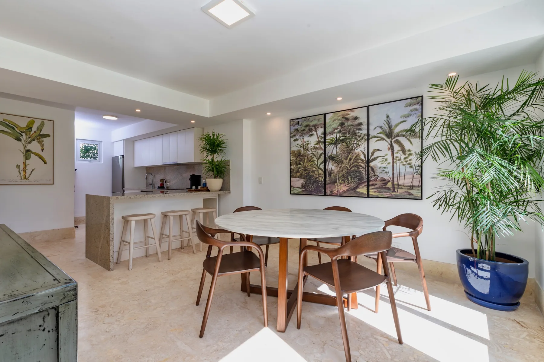 A bright dining area with a round table and several seats beside the kitchen.