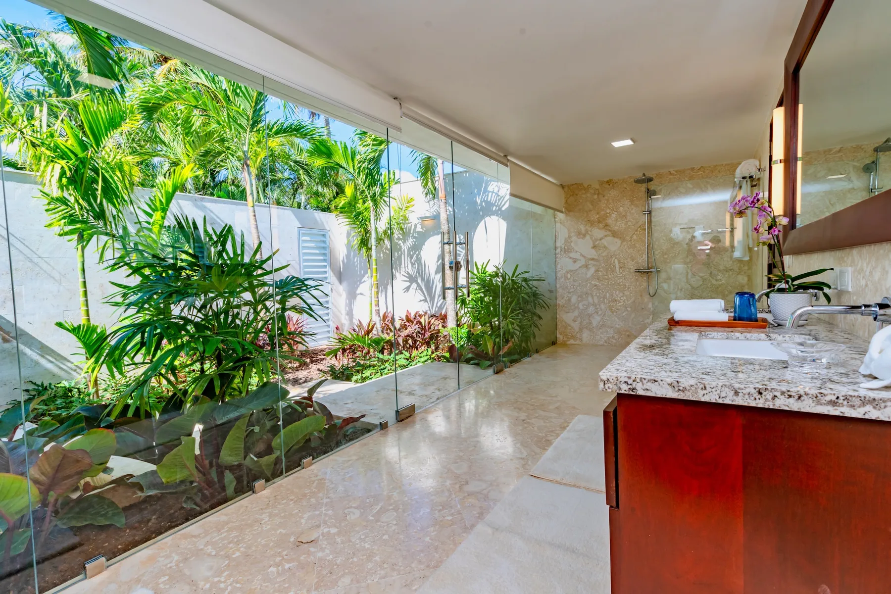 A bathroom vanity and shower area open onto a glass-walled tropical garden.