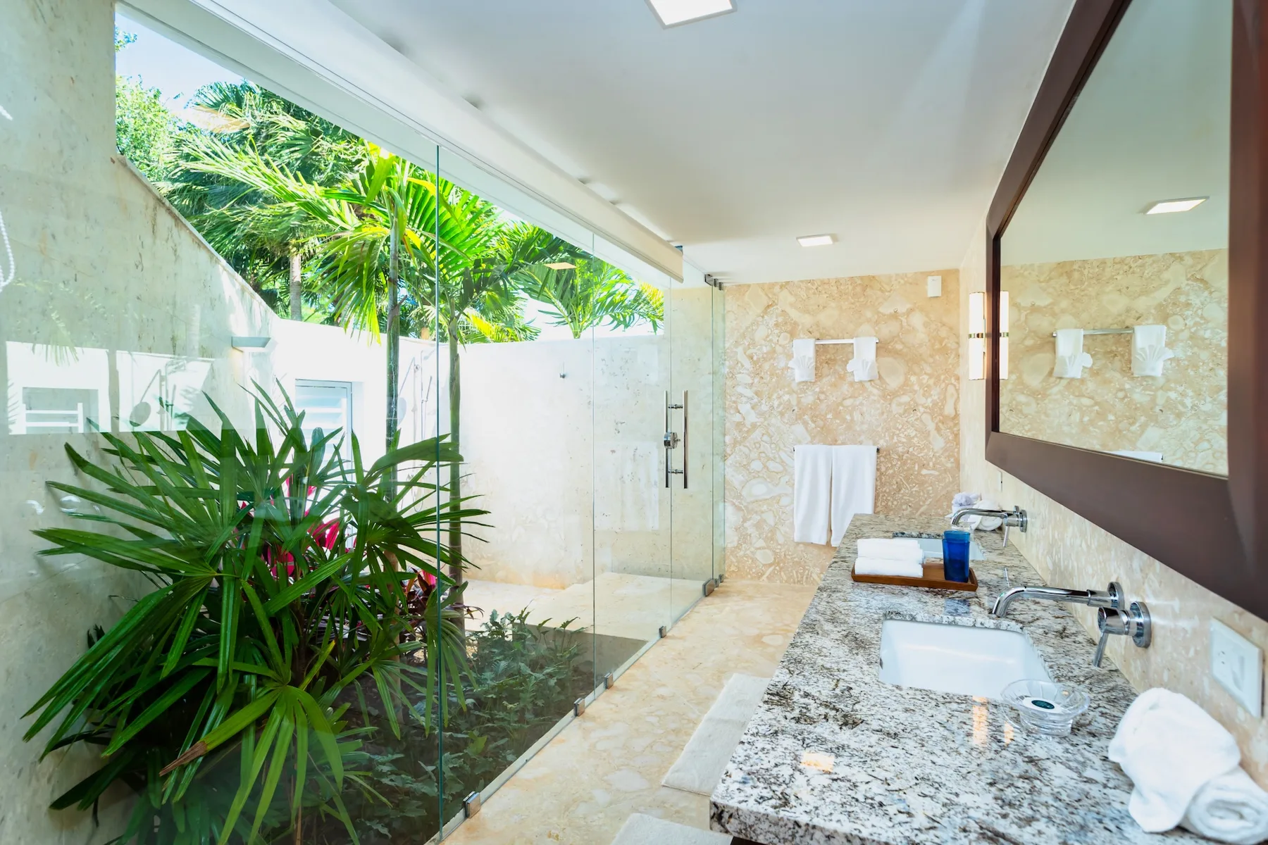 A bright bathroom with a glass shower and a long vanity beside a window.