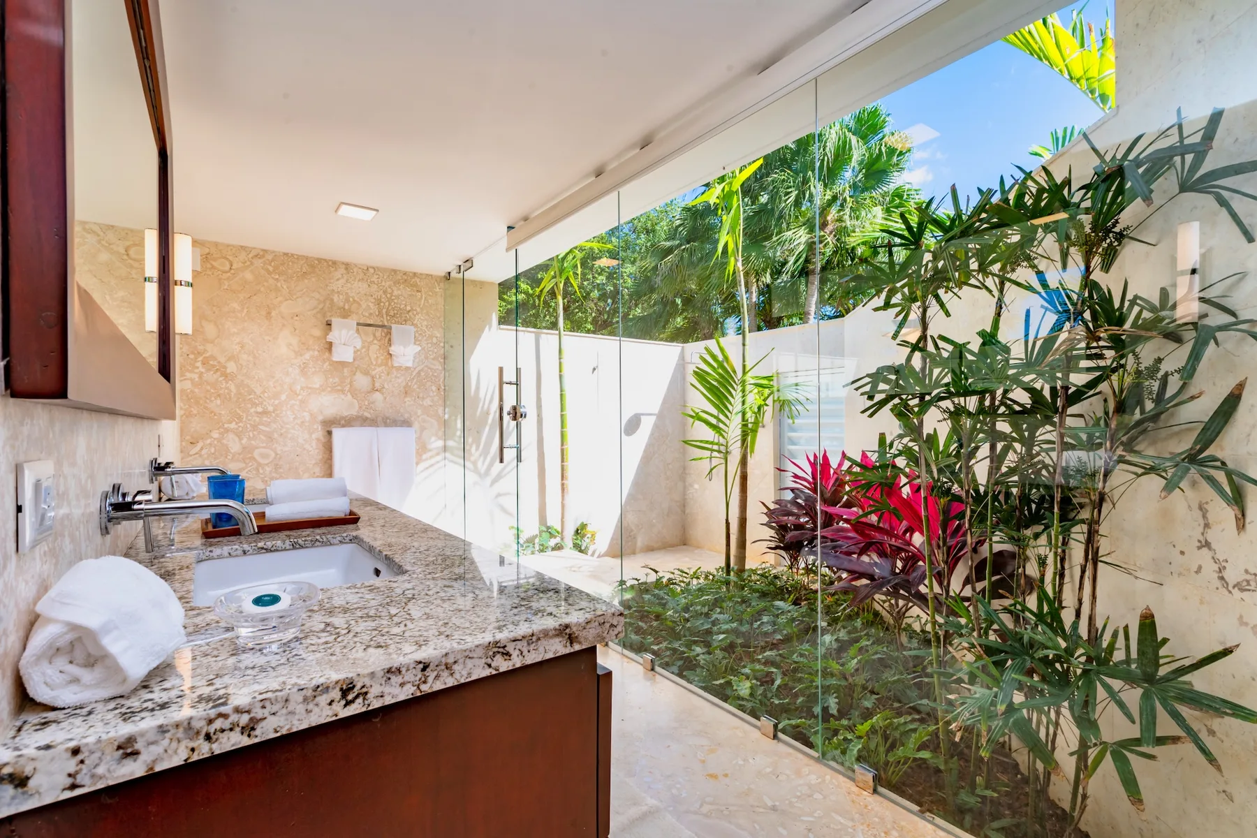 A bathroom vanity and shower open onto a small garden with tropical plants.