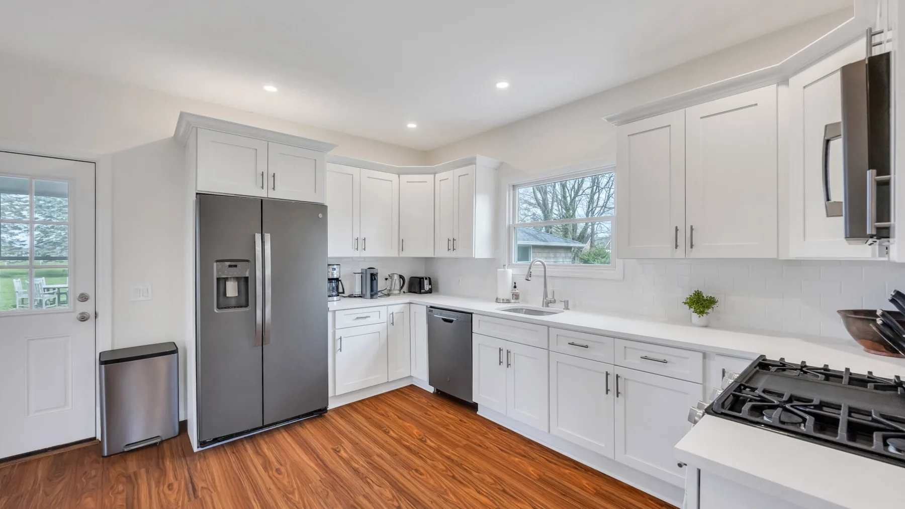 A bright kitchen with white cabinetry, stainless steel appliances, and wood flooring.