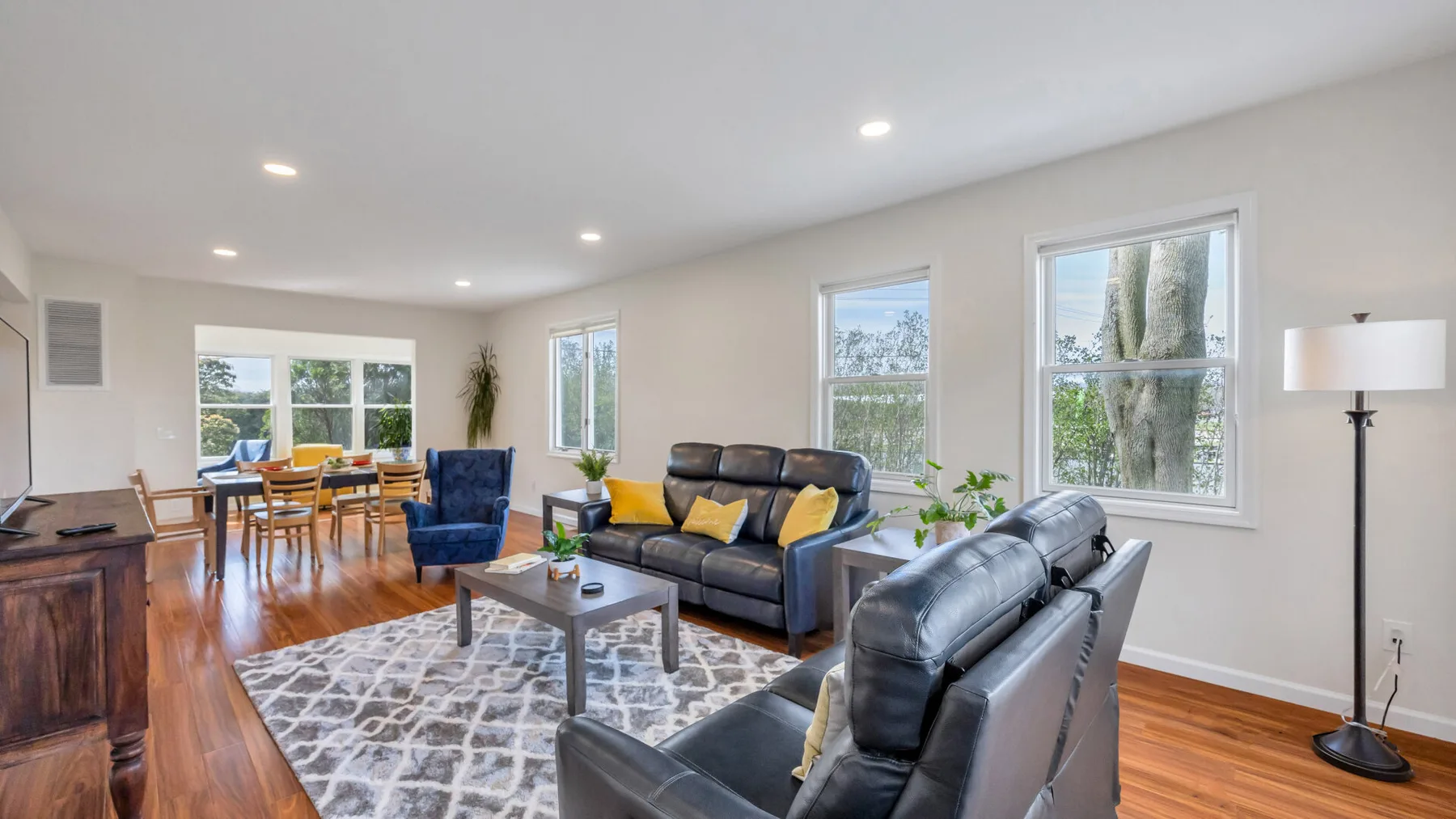 An open living and dining area with dark seating, a dining table, and large windows.