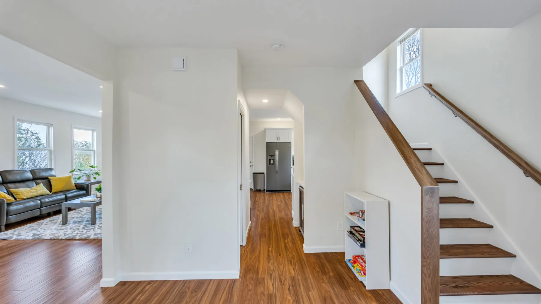 A bright home interior with a wood-floored hallway, staircase, and living area.