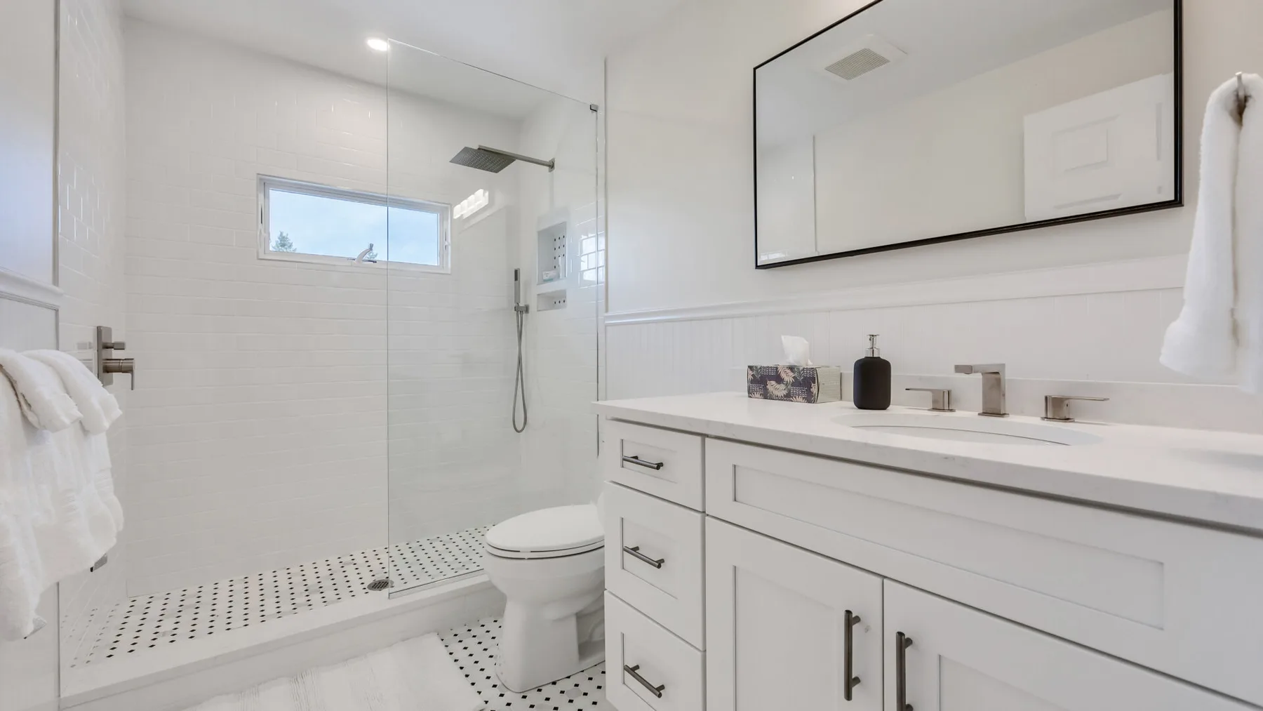 A bright bathroom with a walk-in shower and a long vanity.