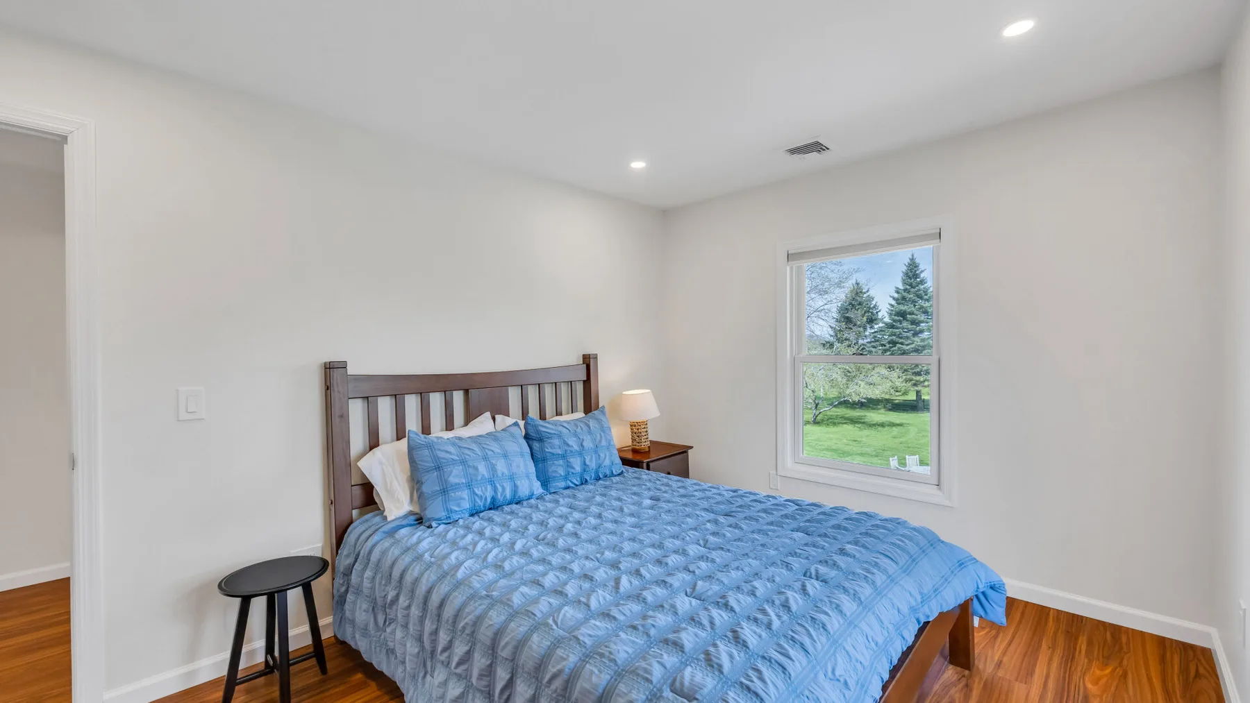 A bedroom with a bed covered in blue bedding and a window overlooking greenery.