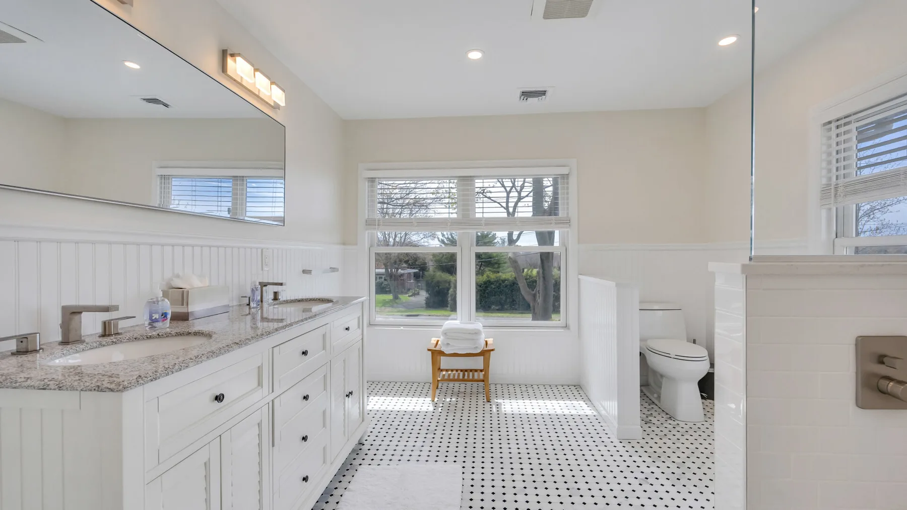 A bright bathroom with a long vanity, large mirror, and window.