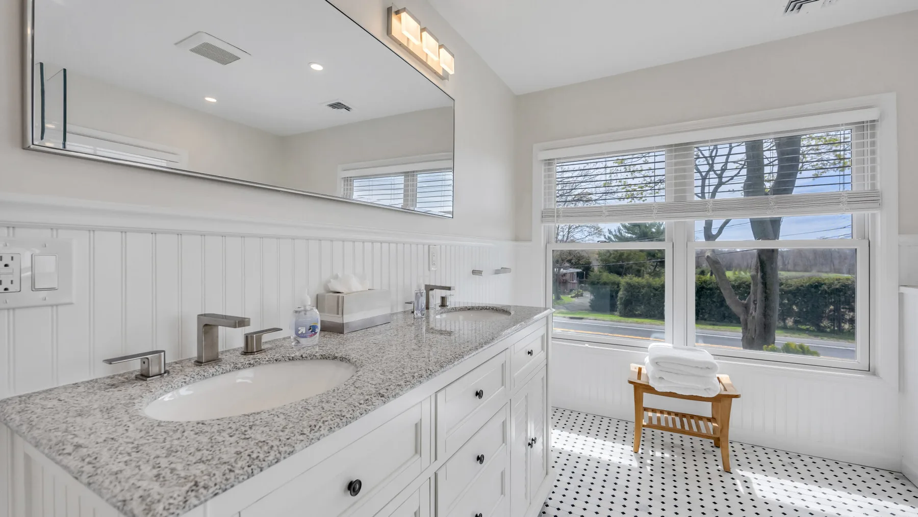 A bright bathroom with a long vanity and a large window overlooking trees.