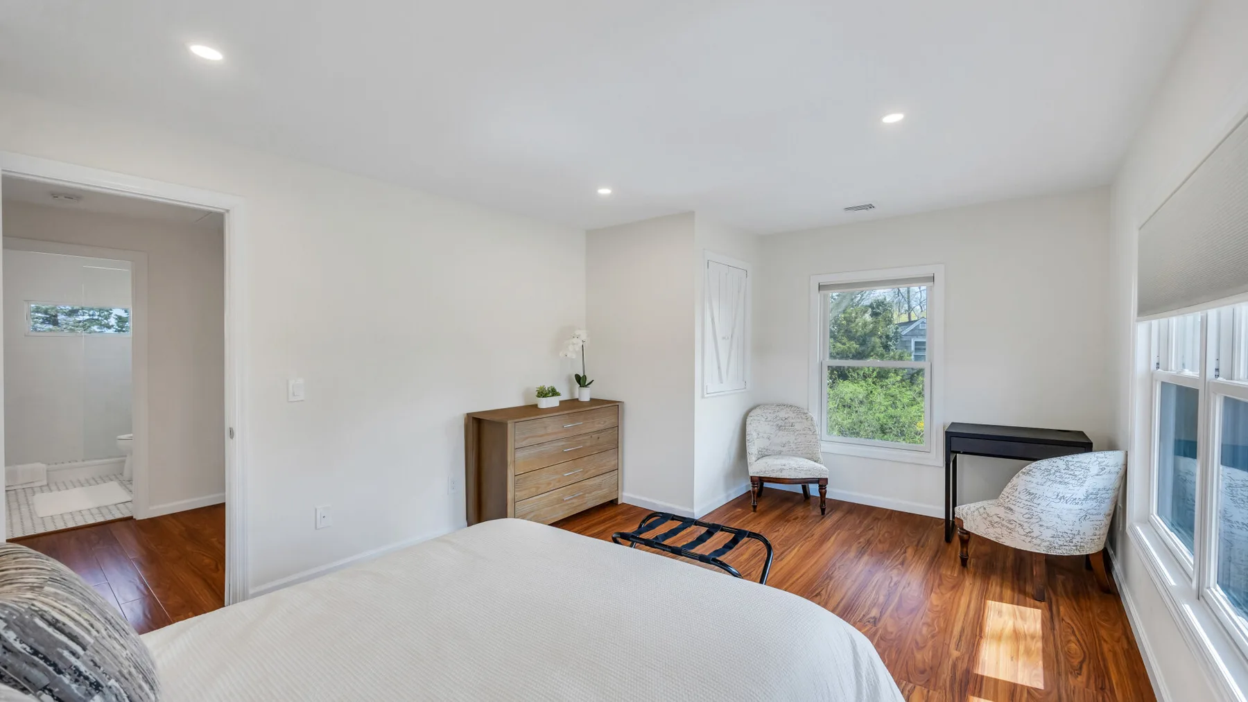 A bright bedroom with a large bed, wooden flooring, and a window.