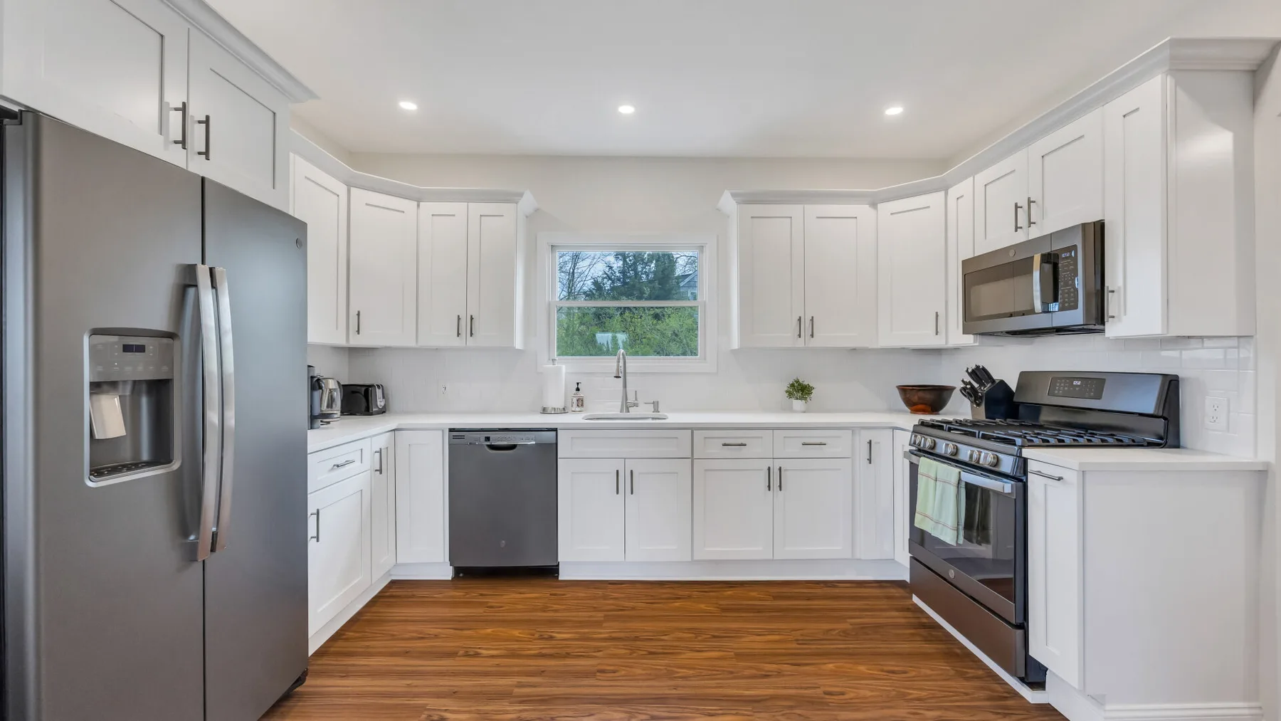 A bright kitchen with white cabinets, stainless steel appliances, and wood flooring.