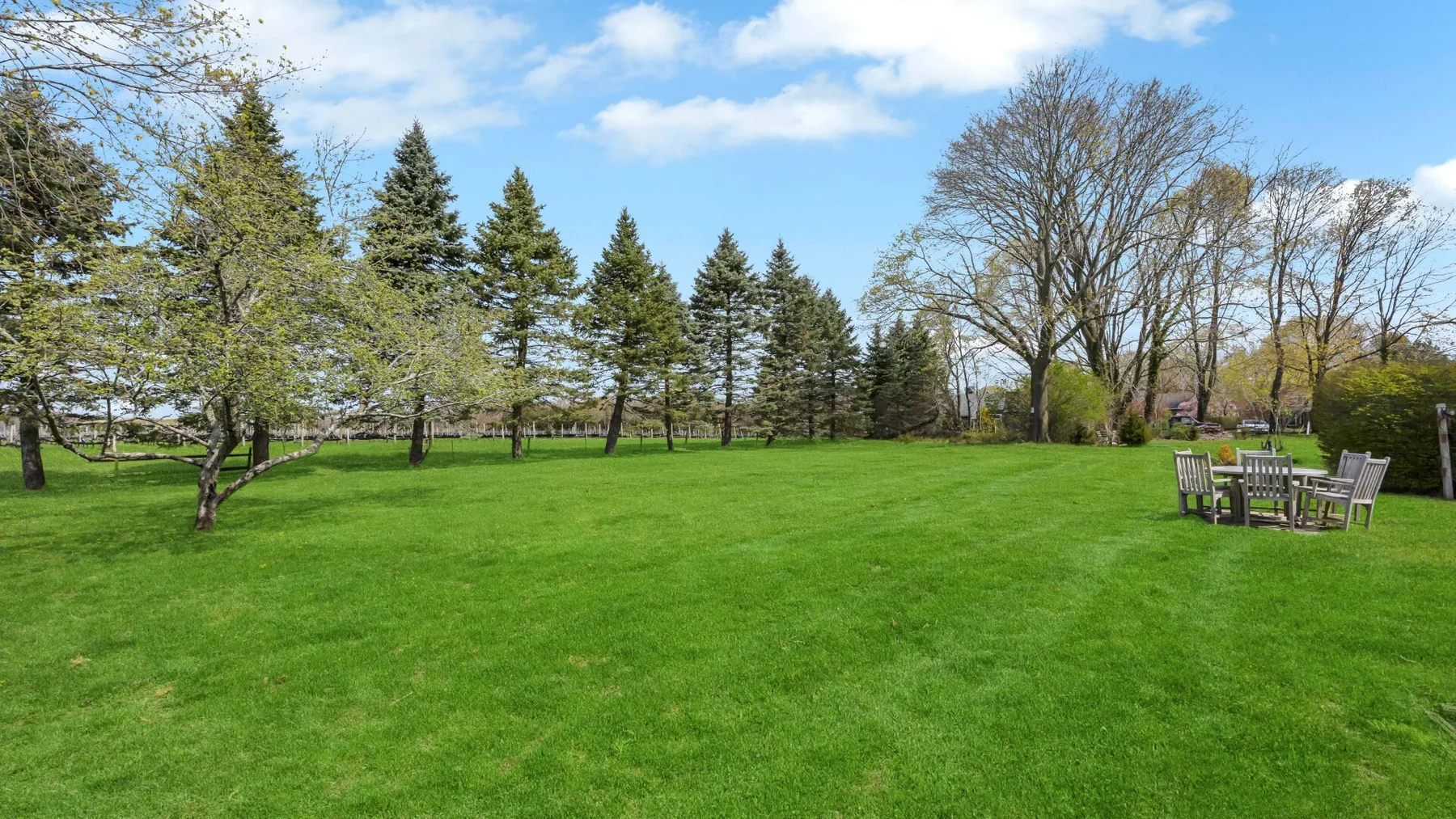 A broad green lawn bordered by trees, with outdoor seating at the edge.