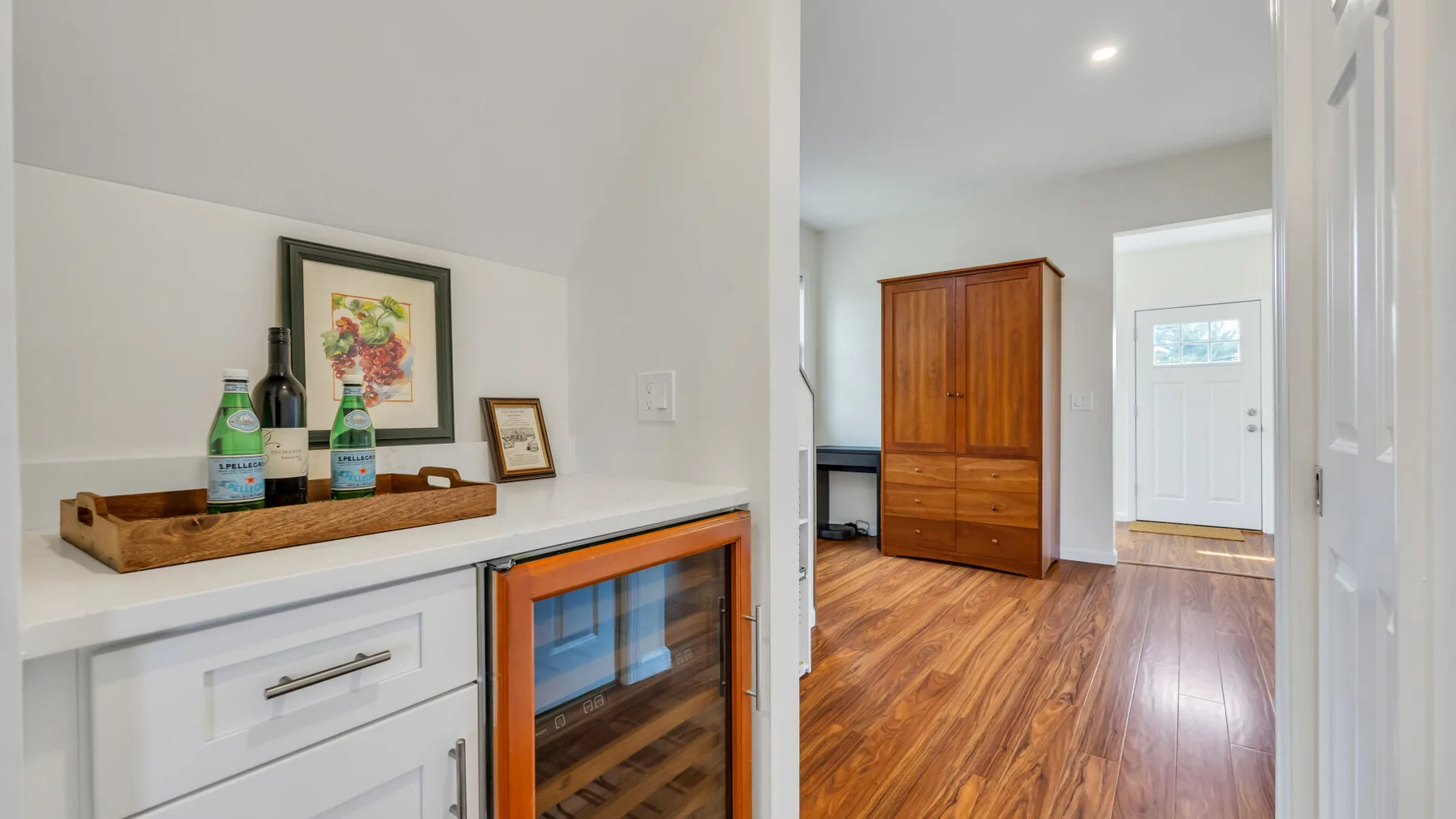 A bright interior hallway with a wooden cabinet and a glass-front beverage cooler.