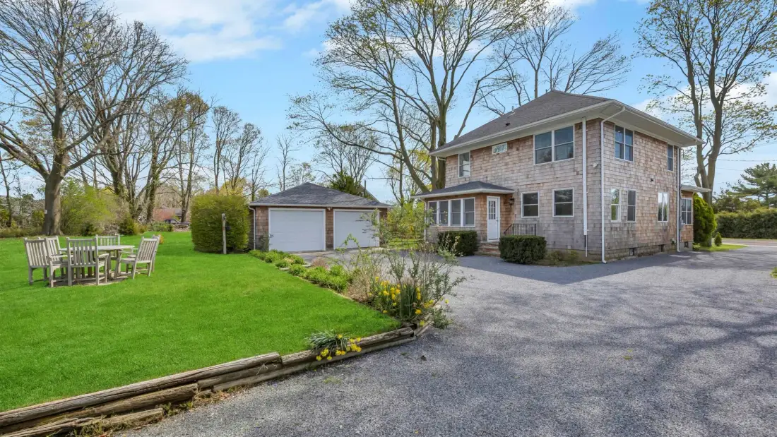 A two-story house and detached garage stand beside a broad lawn and paved driveway.