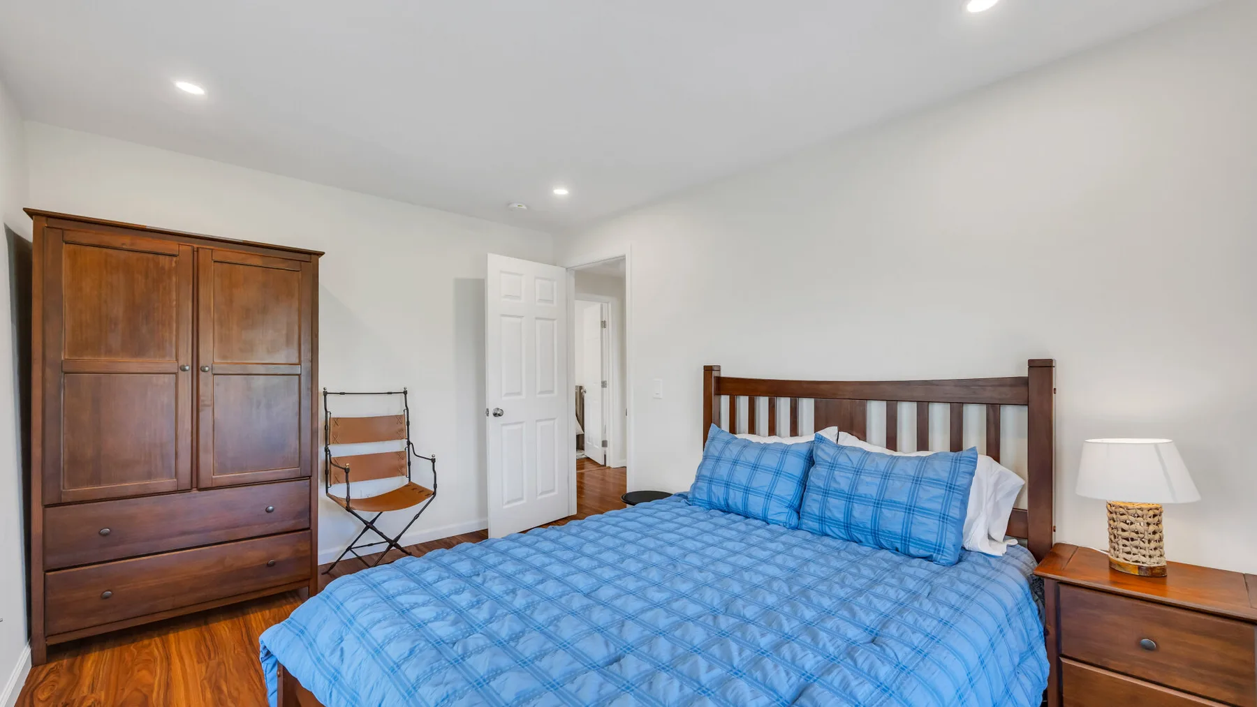 A bedroom with a blue bedspread, wooden wardrobe, and bedside table.
