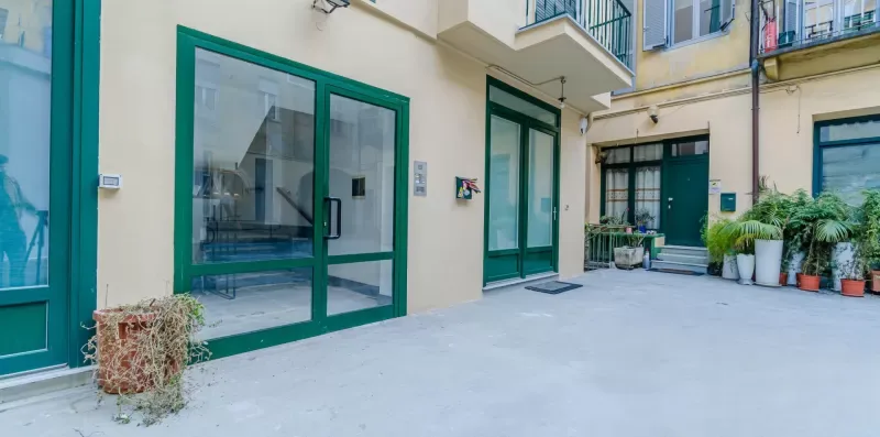A paved courtyard between building entrances, with potted plants along the far wall.
