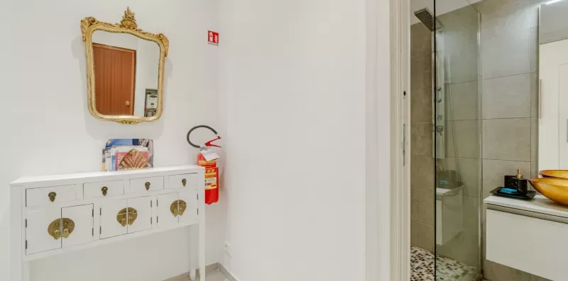 A bathroom vanity with an ornate mirror stands beside a glass-enclosed shower.